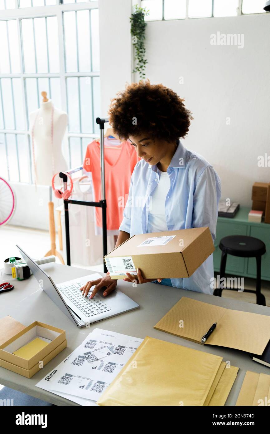 Stilista di moda femminile con computer portatile che utilizza il telefono cellulare mentre lavora in studio Foto Stock