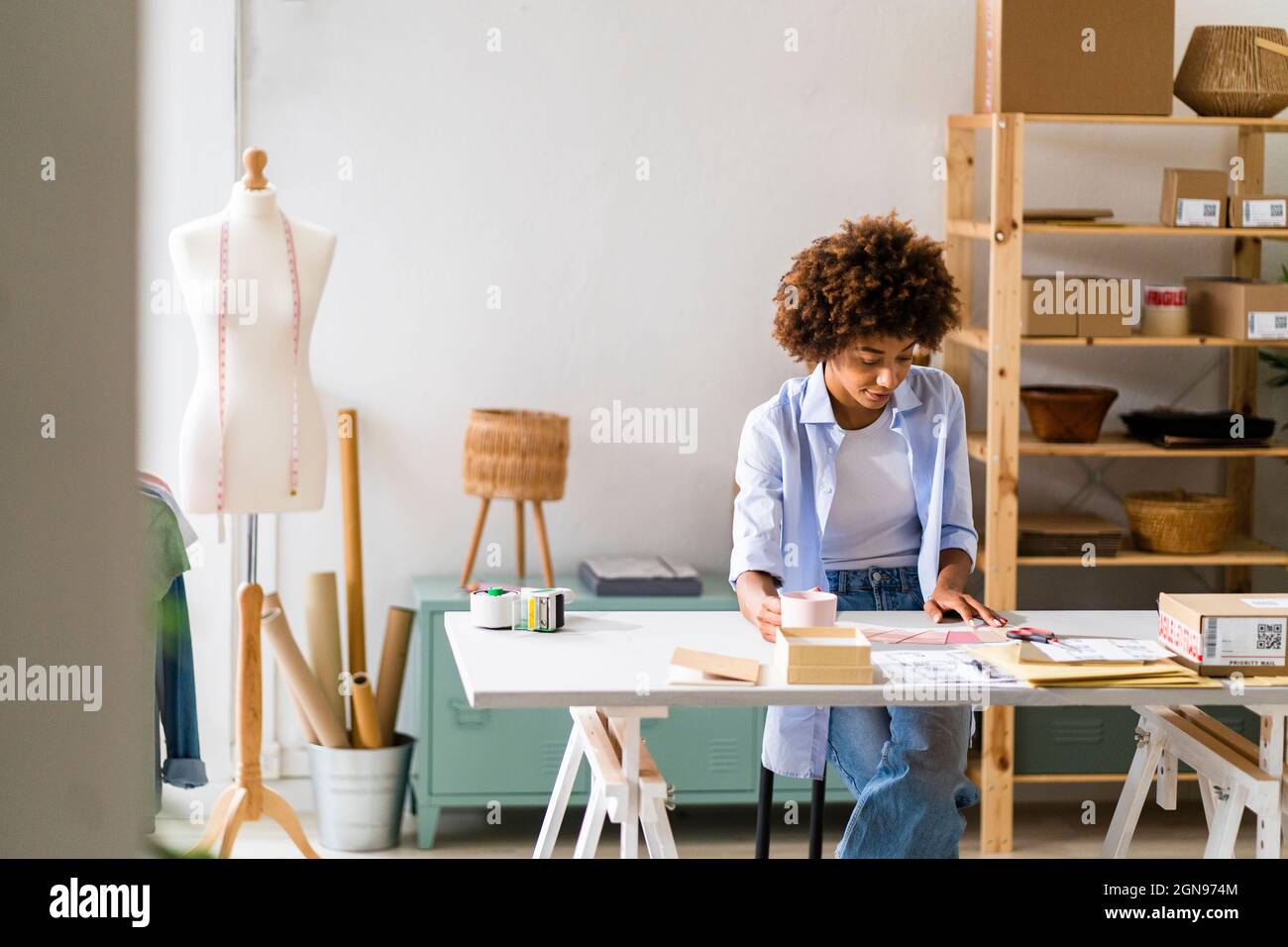 Stilista di moda femminile con tazza seduta alla scrivania in studio Foto Stock
