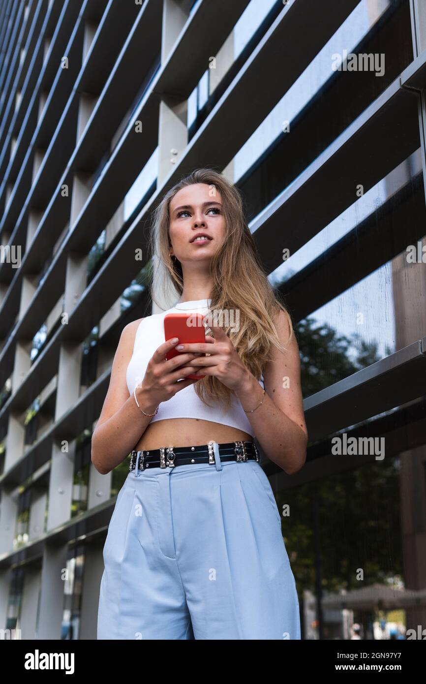 Freelance femminile con telefono cellulare in piedi di fronte all'edificio Foto Stock