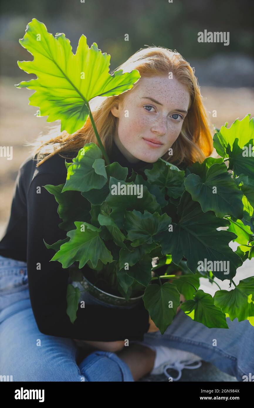 Giovane donna rossa che abbraccia la pianta in vaso Foto Stock