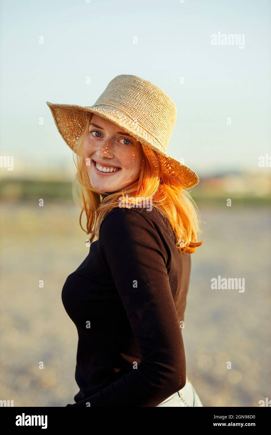 Donna rossa sorridente che indossa un cappello al tramonto Foto Stock
