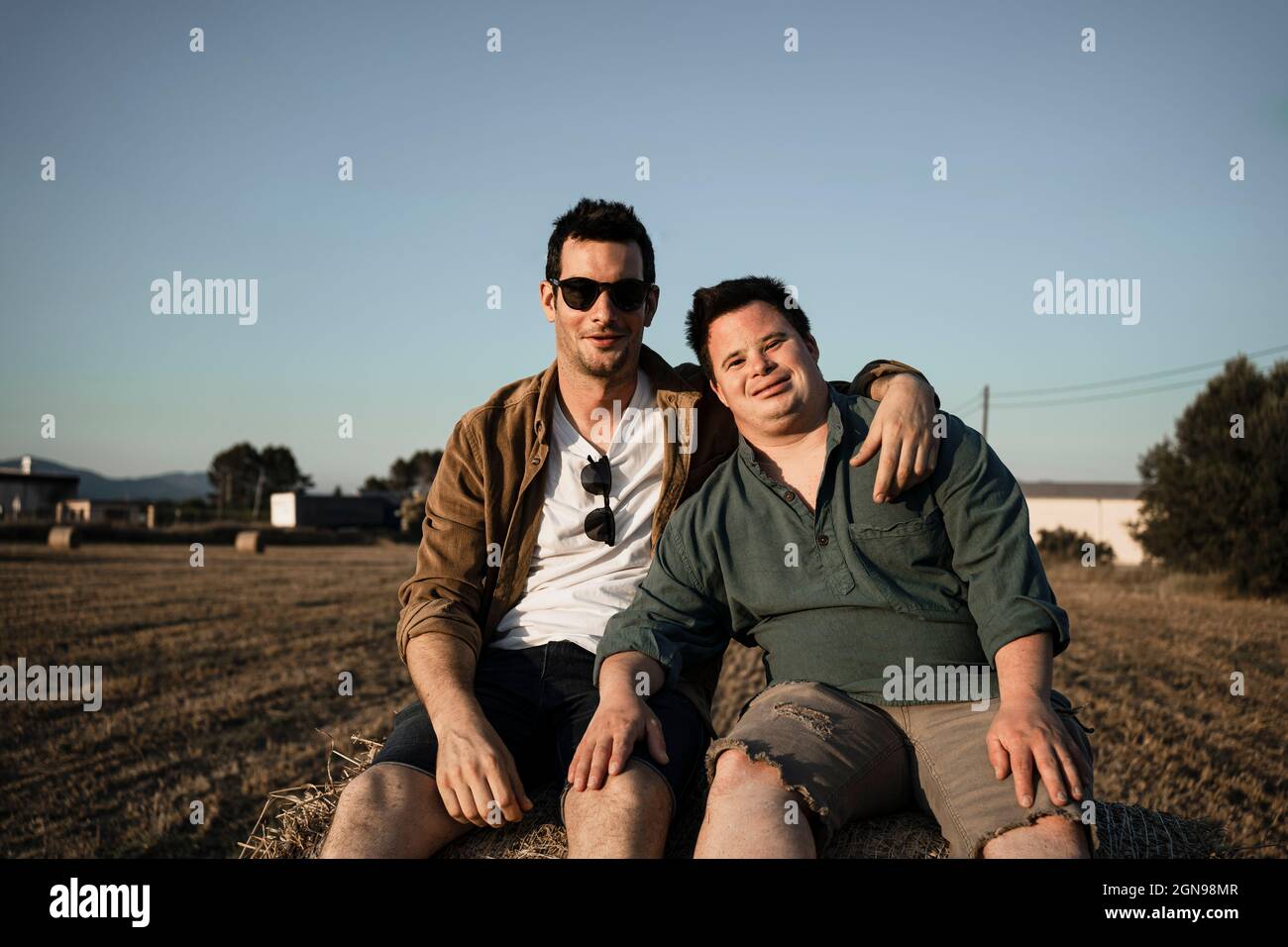 Uomo che indossa occhiali da sole seduti con un amico su una balla di paglia Foto Stock