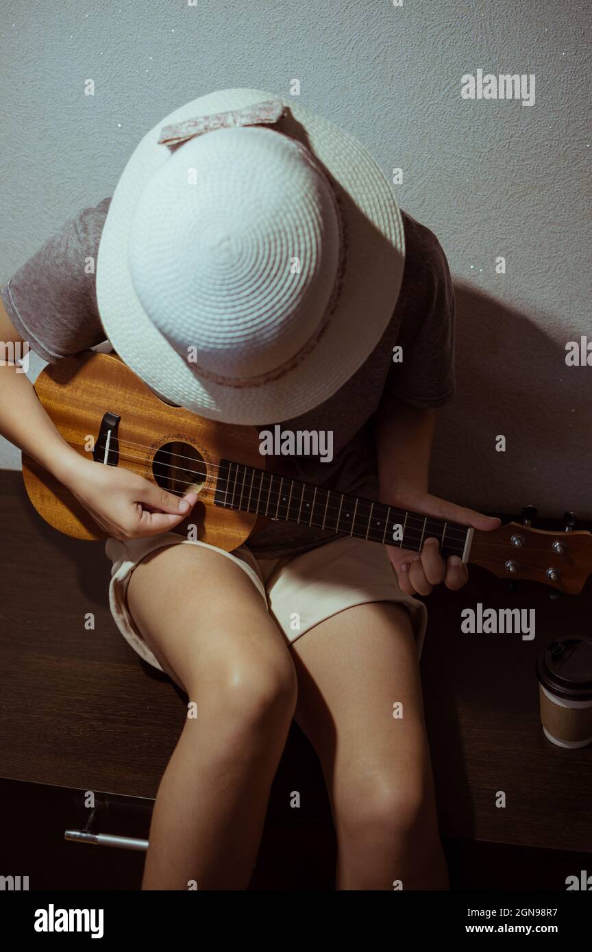 Una ragazza in un cappello di paglia e pantaloncini, giocando l'ukulele piegato sopra Foto Stock