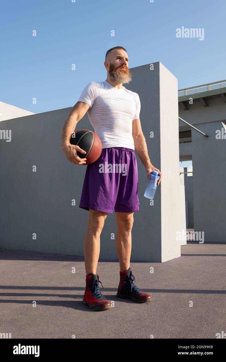 Giocatore di basket professionista che si guarda lontano mentre si sta in piedi vicino ai lavori e riposarsi dopo l'esercizio Foto Stock