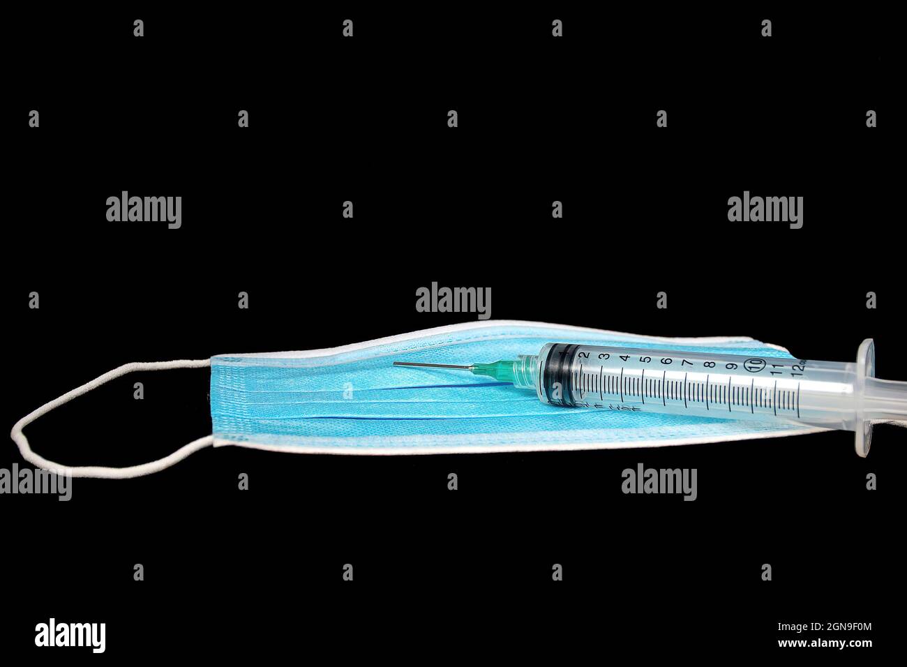 Siringa medica su carta blu usa e getta maschera isolato su nero Foto Stock