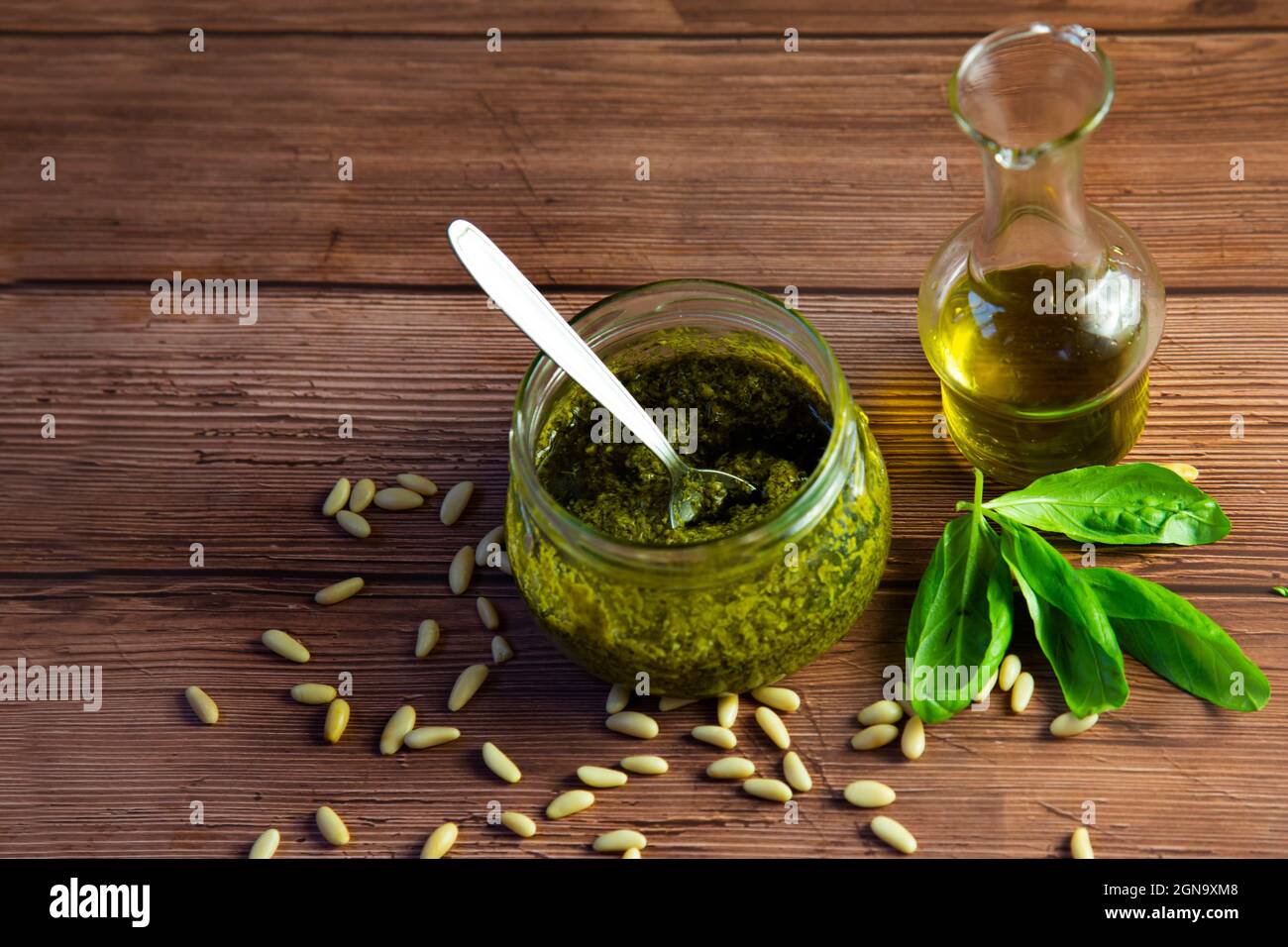 Preparazione del pesto genovese, la salsa pronta nel vaso di vetro, pinoli, olio d'oliva e foglie di basilico Foto Stock