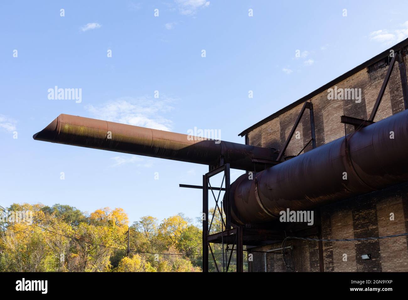 Tubi giganti avvolti e emanati da un vecchio magazzino industriale, paesaggio della stagione autunnale e cieli blu, aspetto orizzontale Foto Stock