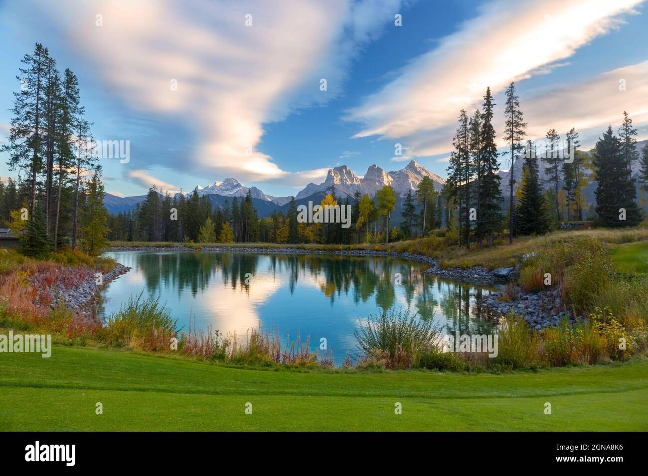 Tempo nuvole riflessi nel campo da golf calma Blue Water Lake. Verde erba distante picchi di montagna orizzonte. Bow Valley, Alberta Banff National Park Foto Stock