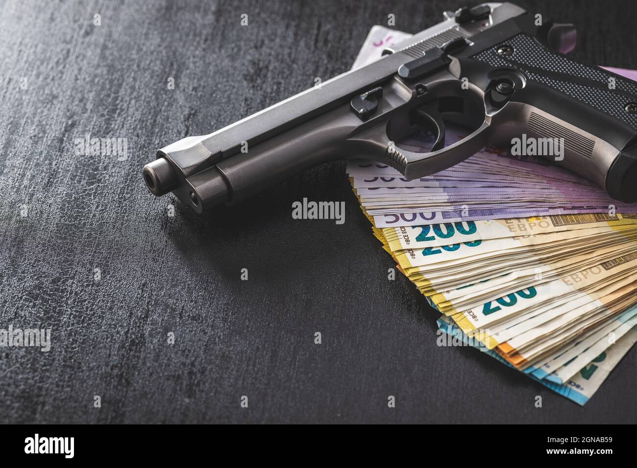 Pistola manuale e banconote in euro su tavola nera. Foto Stock