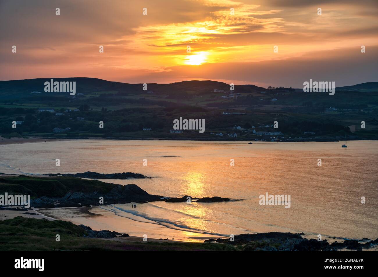 Il sole sorge dietro le montagne alla spiaggia di Culdaff nella contea di Donegal in Irlanda Foto Stock
