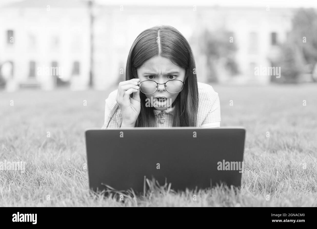 OH no. Torna a scuola. Teen girl usa il computer su erba verde nel parco. Bambino in occhiali con notebook. Nuova tecnologia nella vita moderna. Studio. Sorpreso Foto Stock