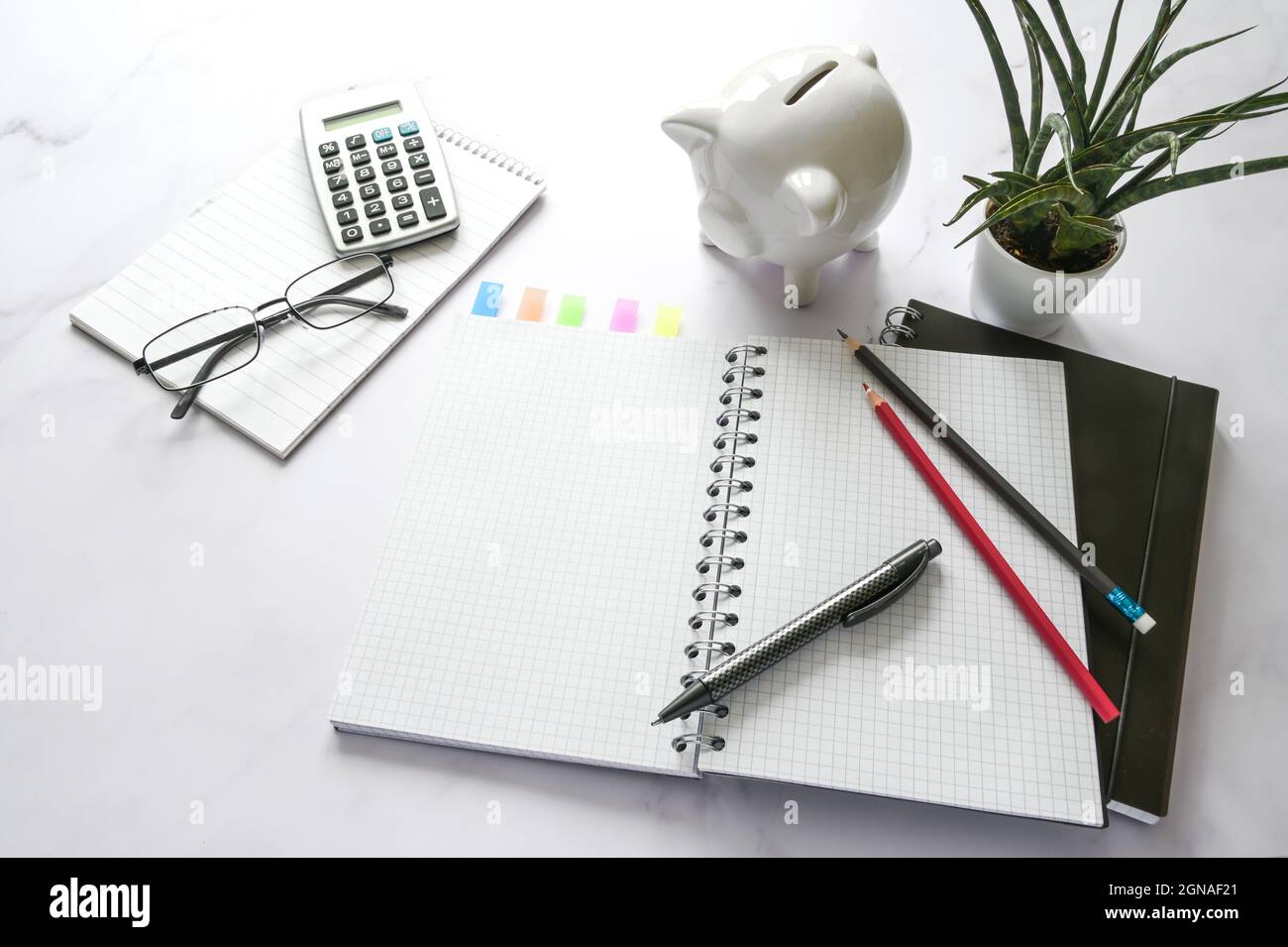 Scrivania da ufficio con un notebook vuoto, banco di porcellini, calcolatrice e accessori fissi su una superficie in marmo, spazio per la copia, messa a fuoco selezionata, profondità di fuoco ridotta Foto Stock