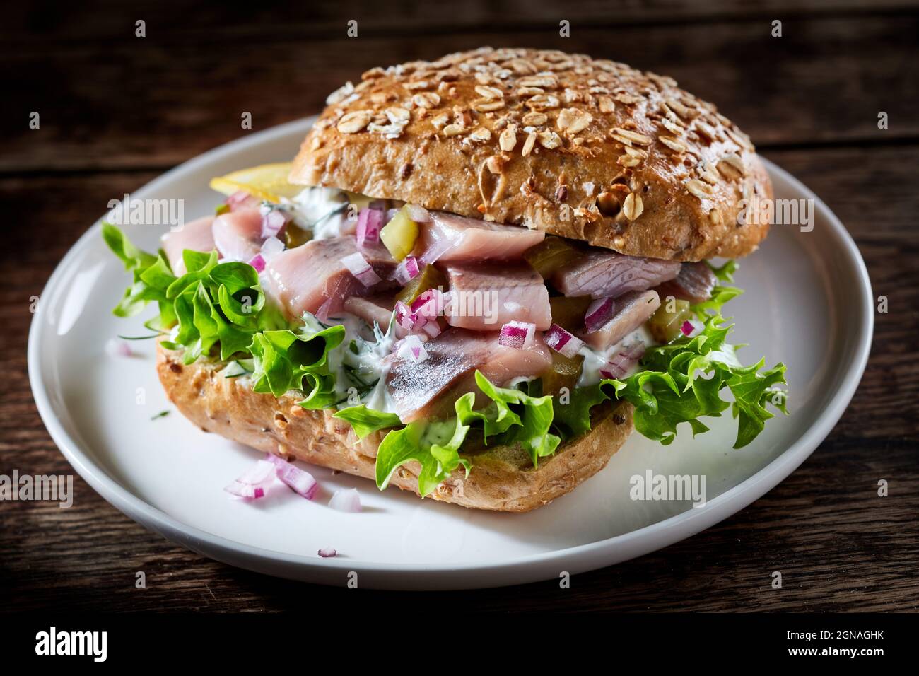 Alto angolo di panino di pesce con aringhe e verdure tritate servite su piatto su sfondo di legno Foto Stock