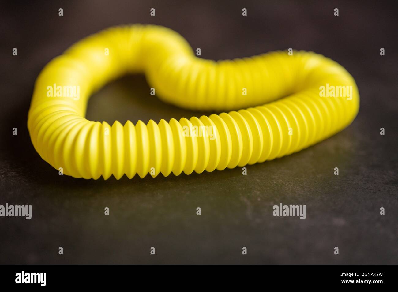 bambini anti stress sensoriale pop tubo di plastica fidget push giocattolo su un tavolo nero o sfondo pavimento. bambini piccoli pop tube giocattoli giallo tonalità chiaro, Foto Stock