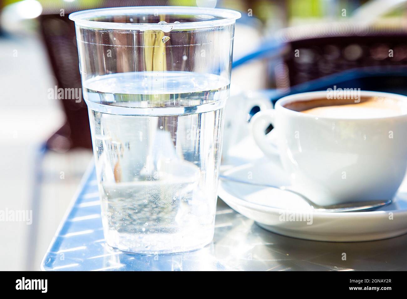 Vetro trasparente di plastica con acqua e tazza di cappuccino e tavolini di caffe sullo sfondo sfocati. Caffè servito in stile italiano tradizionale. Ancora Foto Stock