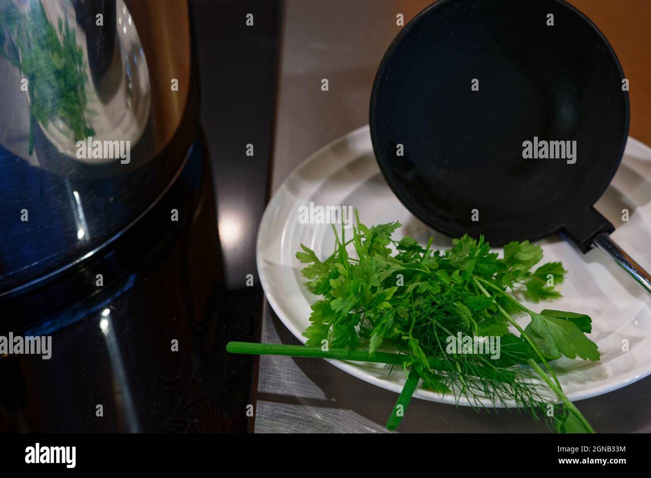 Le erbe verdi si siedono su un piatto con un mestolo della zuppa, stanno aspettando di essere aggiunte alla pentola della zuppa. Foto Stock