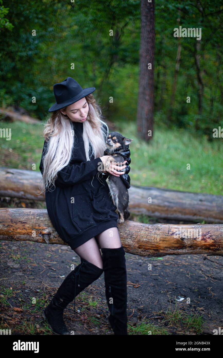 Giovane donna bianca con capelli biondi nella foresta con un cane piccolo Foto Stock