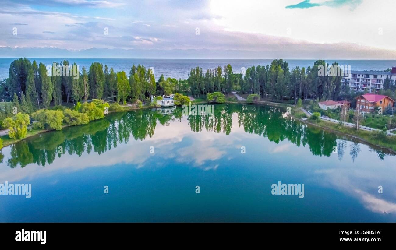 Idilliaco paesaggio estivo con lago vicino alla montagna con riflessi dalle nuvole e dalla foresta. Issyk kul, Kirghizistan. Foto Stock