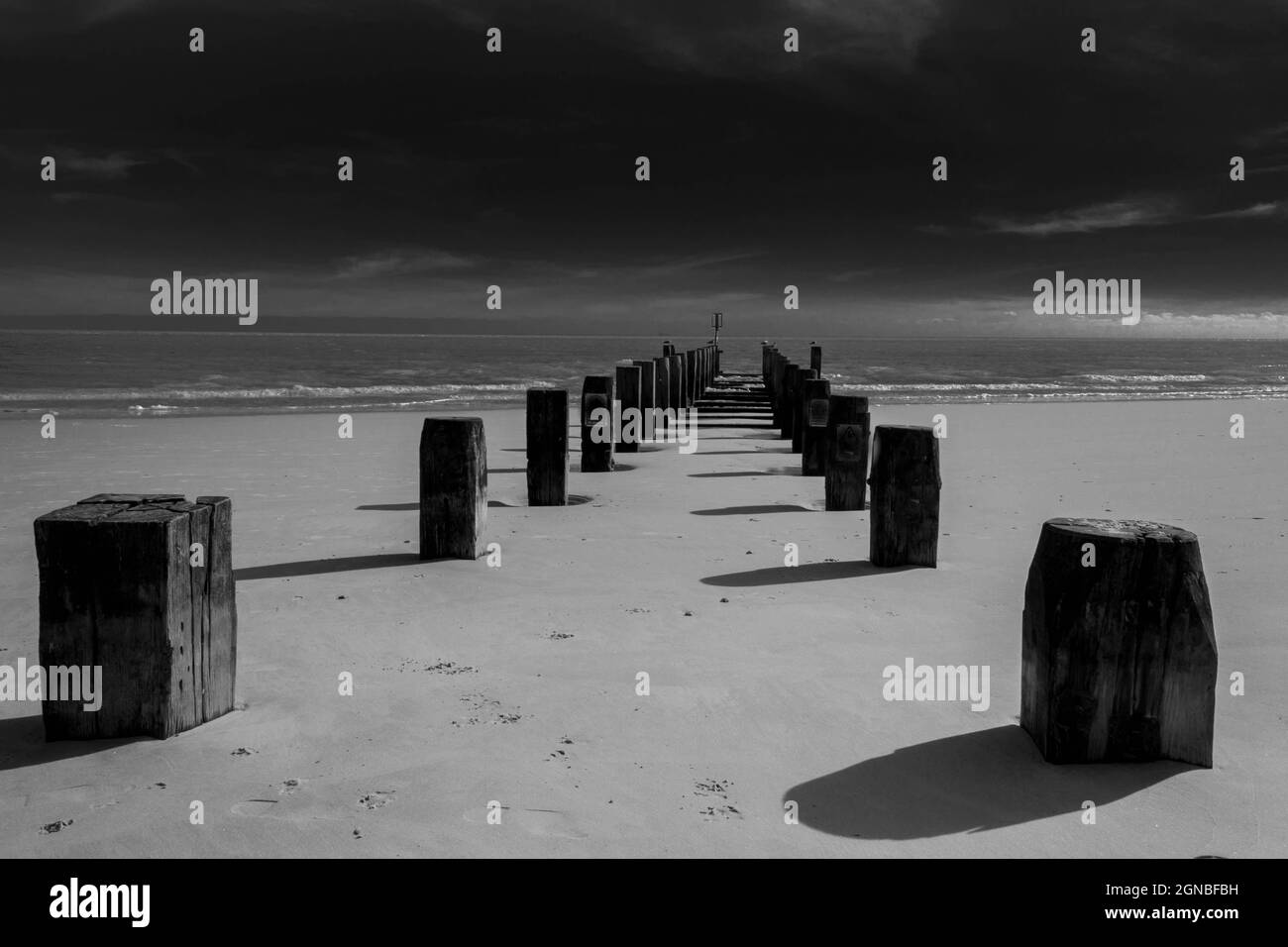 Immagine in bianco e nero di vecchi groynes, onde e sabbia sulla spiaggia di Lowestoft Suffolk UK. Nessuna gente Foto Stock
