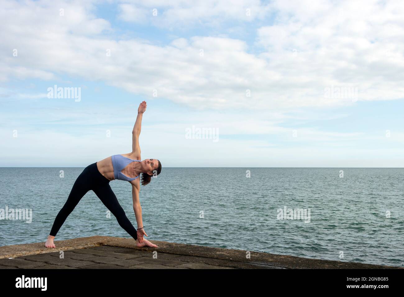 Donna attraente che pratica yoga sul mare, posa Triangolo. Foto Stock