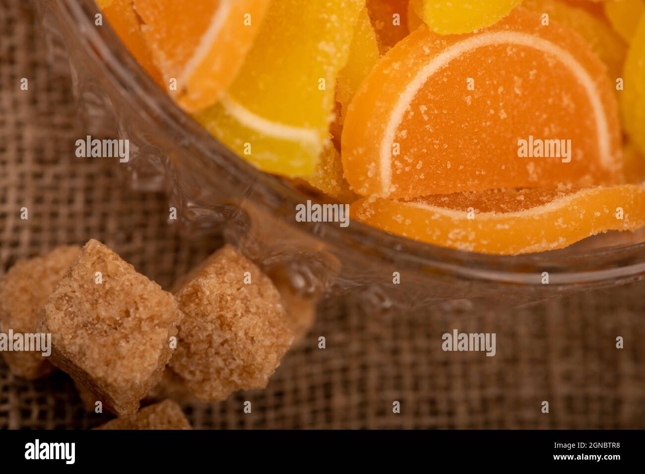 Fette di limone di marmellata multicolore in vaso di vetro e pezzi di zucchero di canna di canna, primo piano, fuoco selettivo Foto Stock