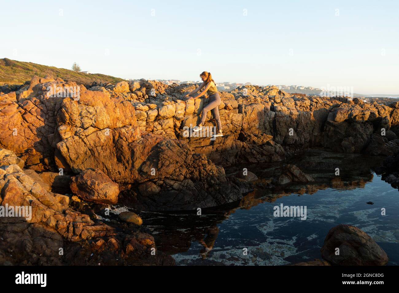 Ragazza adolescente che arrampica le rocce sopra una rockpool sulla costa a De Kelders. Foto Stock