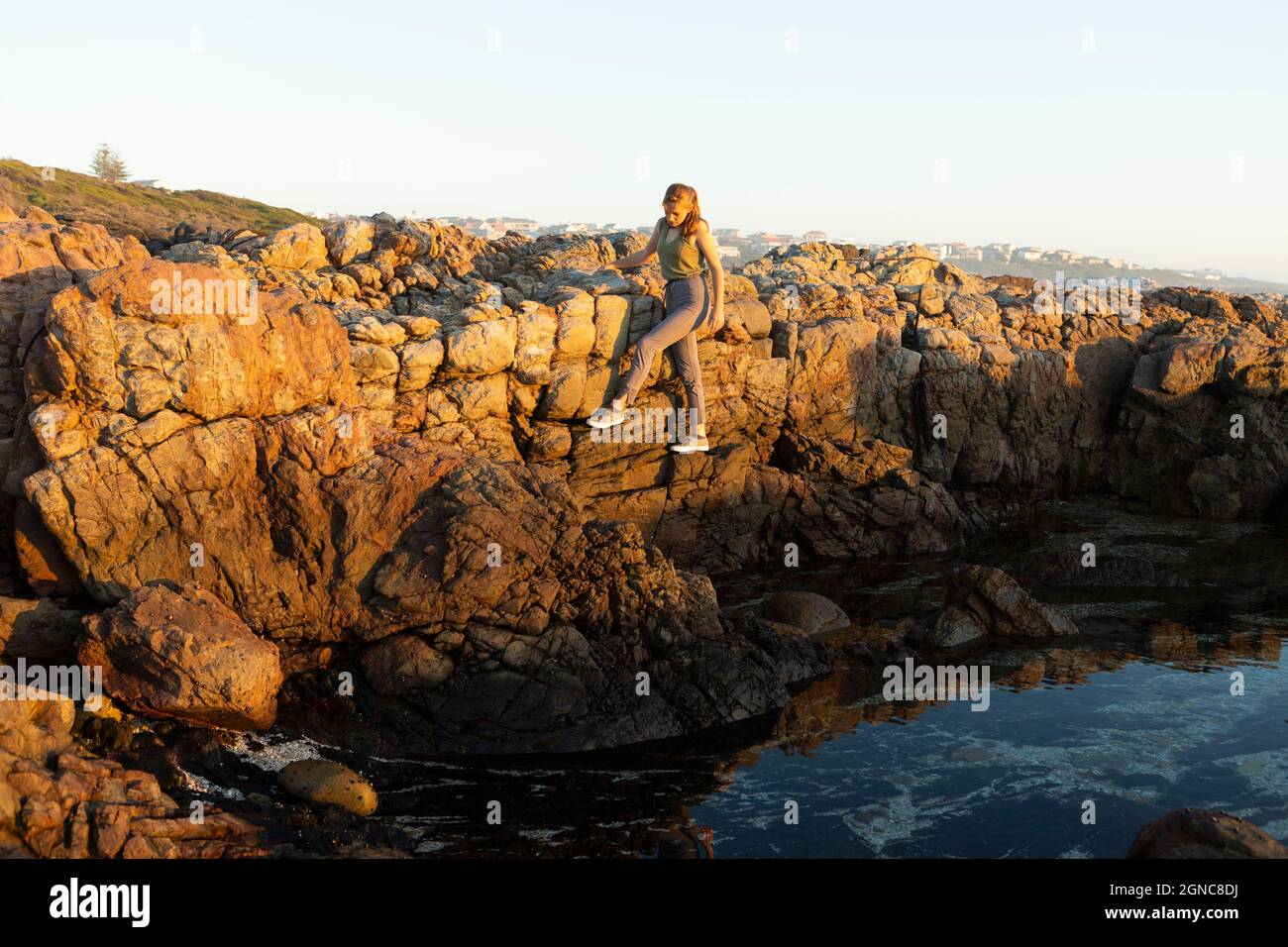 Ragazza adolescente che arrampica le rocce sopra una rockpool sulla costa a De Kelders. Foto Stock