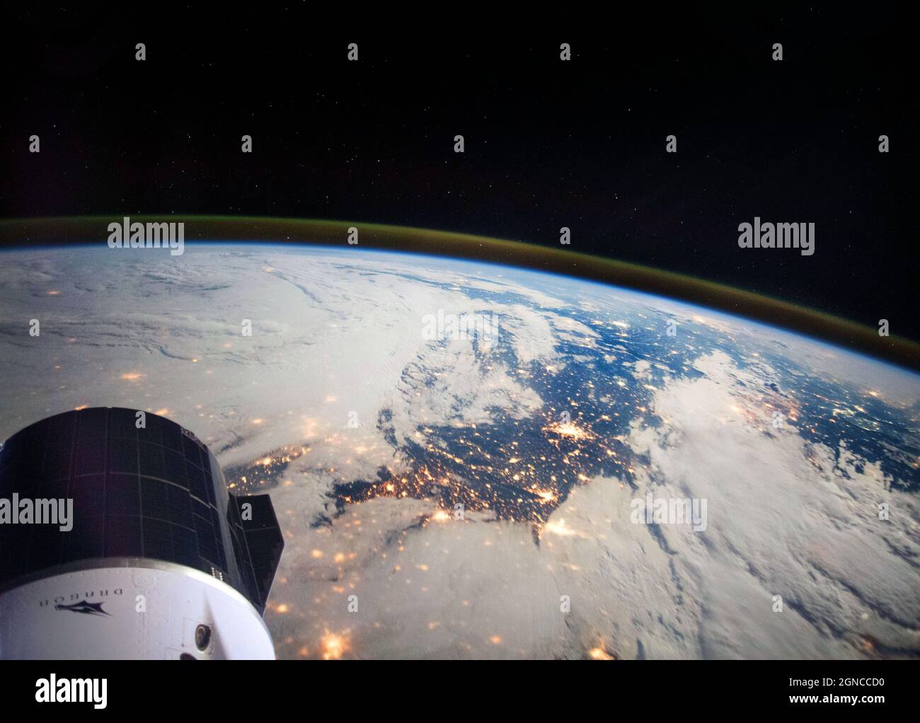 Una parte del veicolo SpaceX Cargo Dragon è raffigurata in basso a sinistra, mentre la Stazione spaziale Internazionale (ISS) orbitava a 264 miglia sopra il nord della Francia. La fotografia a lunga esposizione rivela anche il bagliore atmosferico della Terra e le stelle sopra l'orizzonte. Una versione ottimizzata e potenziata digitalmente di un'immagine NASA / credito NASA. Foto Stock