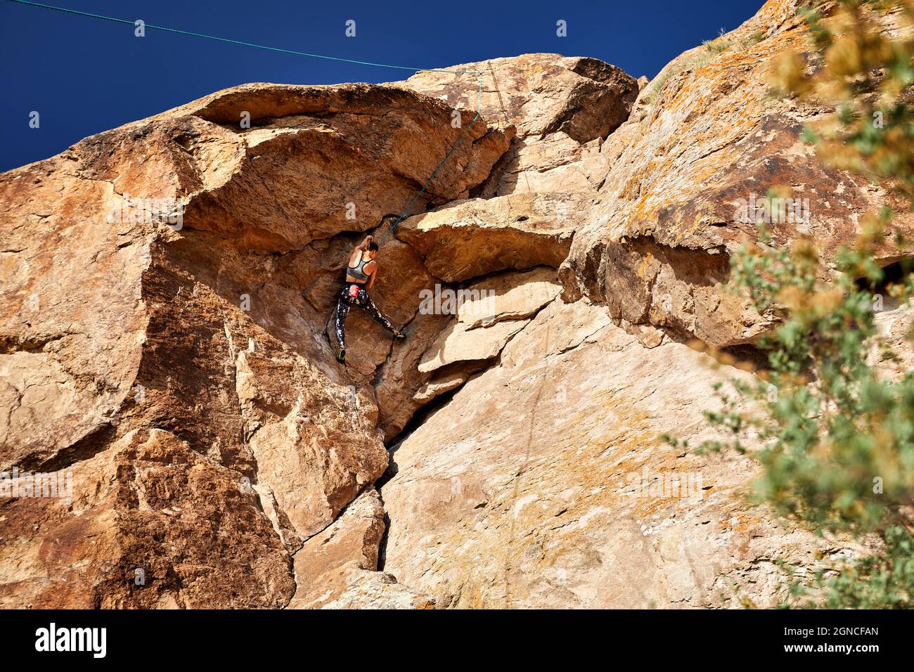 La giovane atleta sta arrampicando sull'alta roccia al tramonto vicino al fiume Ili in Kazakistan Foto Stock