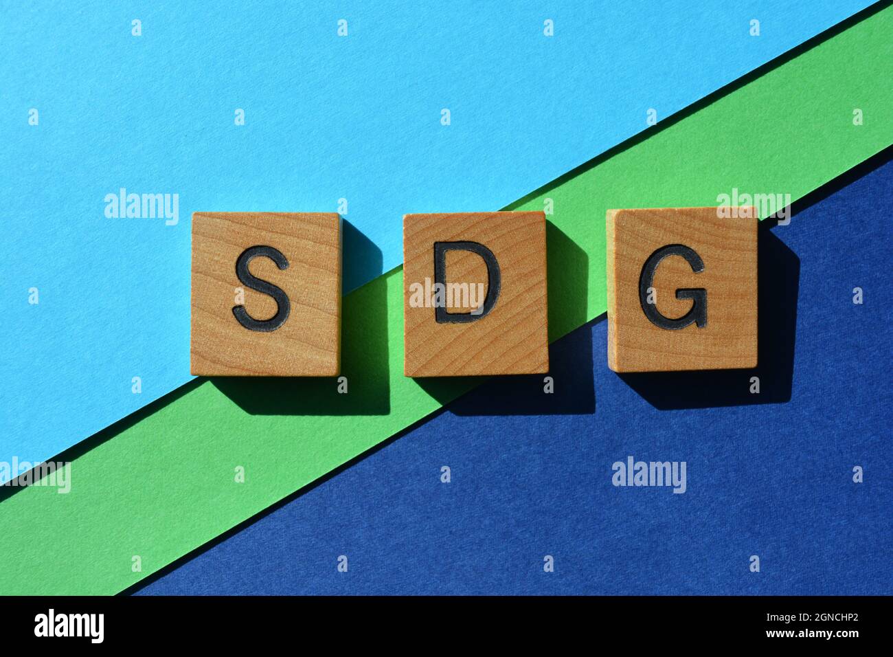 SDG, acronimo di Sustainable Development Goals, in lettere in alfabeto di legno isolate su sfondo verde e blu Foto Stock