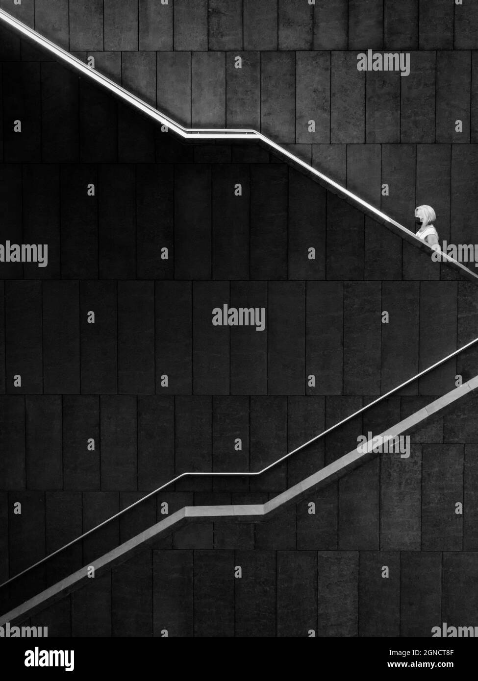 Una donna bionda che sale i gradini di una grande scala di un edificio di architettura contemporanea a Madrid. Foto Stock