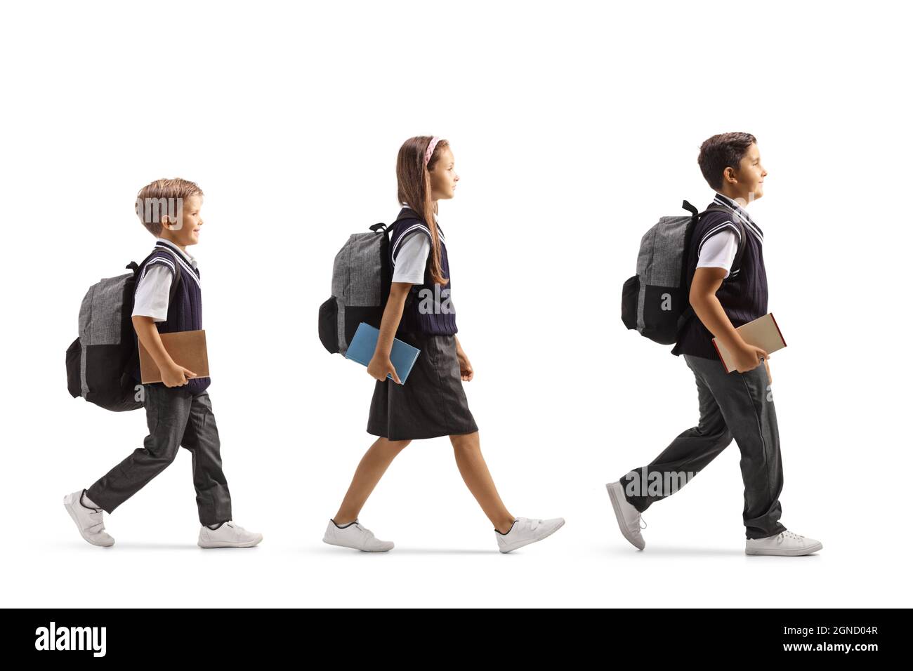 Sparo di profilo completo di una scolgirl e di due scolari che camminano in linea con i libri nelle loro mani isolato su sfondo bianco Foto Stock
