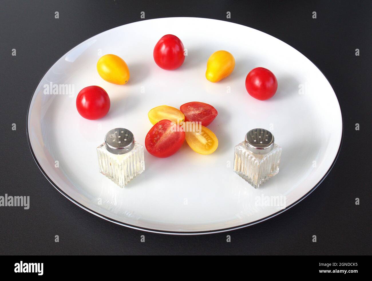 Un po' di pomodori da cocktail con sale e pepe, disposti su un piatto bianco. Foto Stock