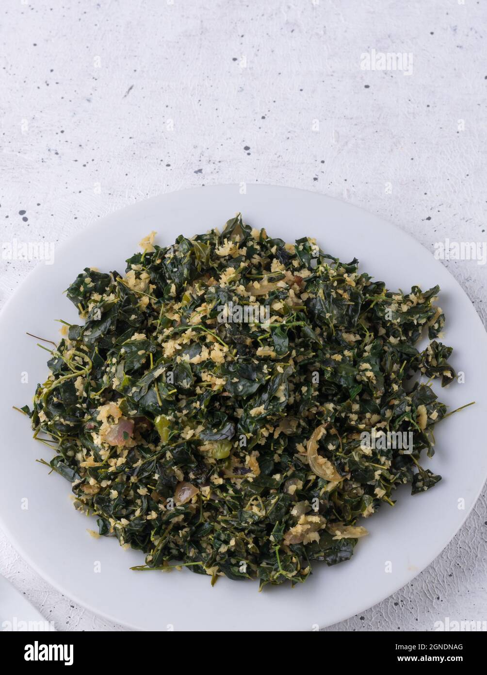 piatto di foglie di moringa o di bastone, mescolato con cocco grattugiato e temperato con olio, piatto vegetariano sano su un piatto, closeup Foto Stock