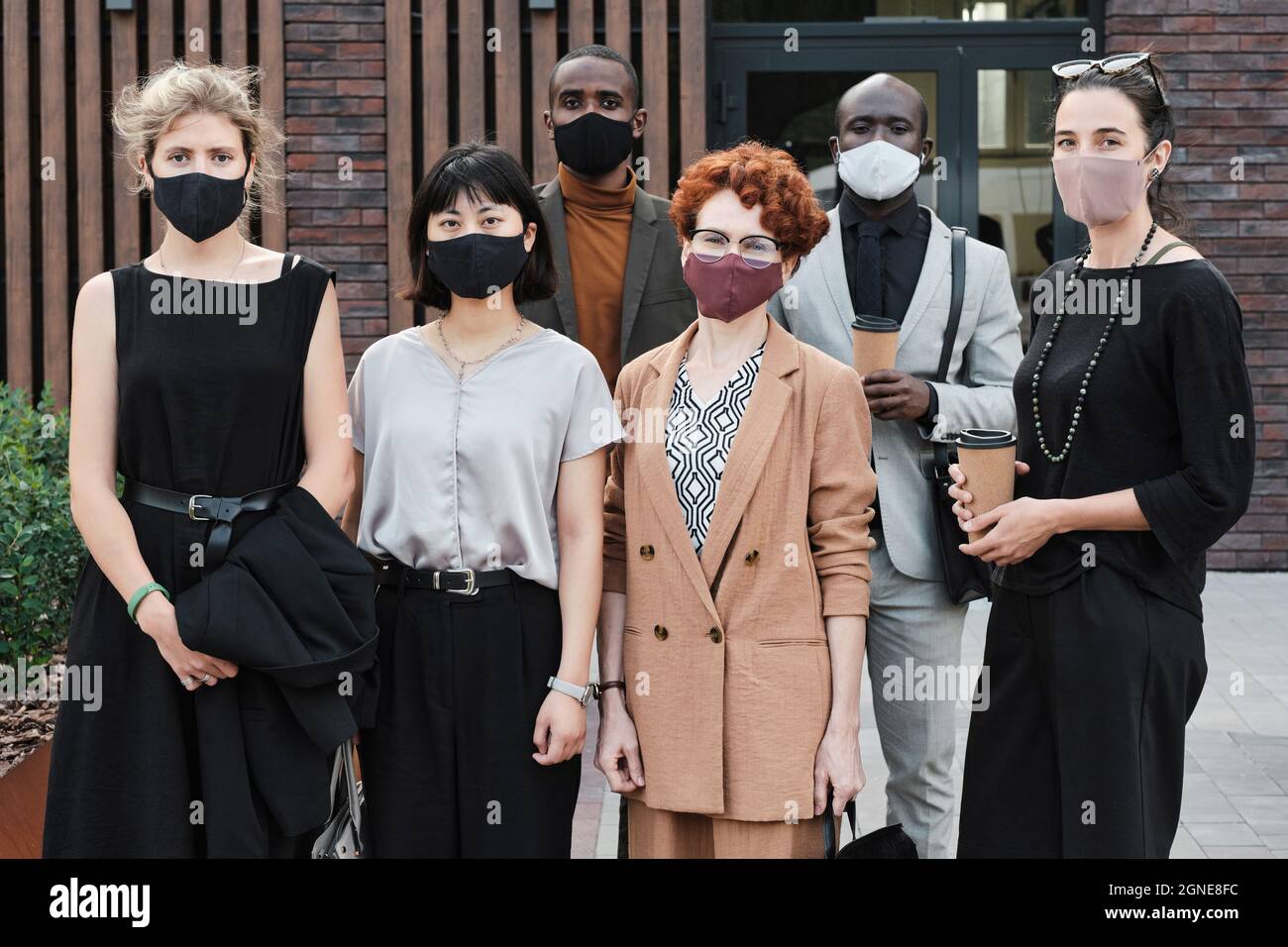 Ritratto di gruppo orizzontale medio lungo girato di uomini e donne multietnici irriconoscibili che indossano maschere protettive sui volti guardando la macchina fotografica Foto Stock
