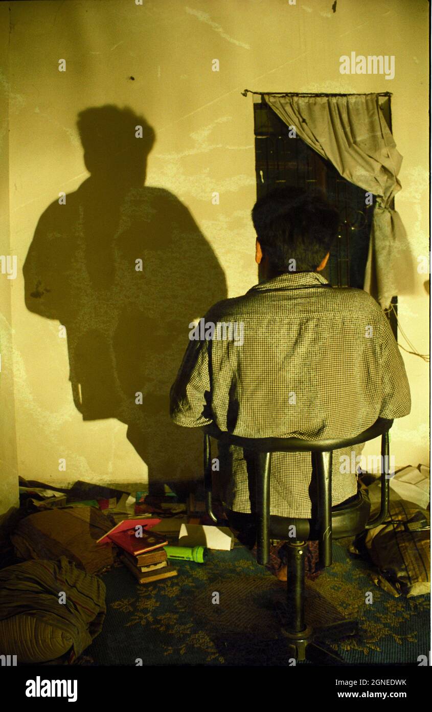 Un uomo che legge un libro con un mucchio di libri sul tavolo accanto a lui. Bangladesh. Foto Stock