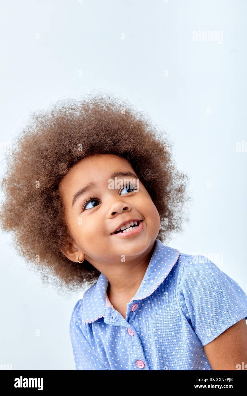 primo piano ritratto di carino sorprendo ragazza africana bambino in t-shirt blu guardando a qualcosa di interessante, ragazza che ha capelli ricci soffici, sorridente hap Foto Stock