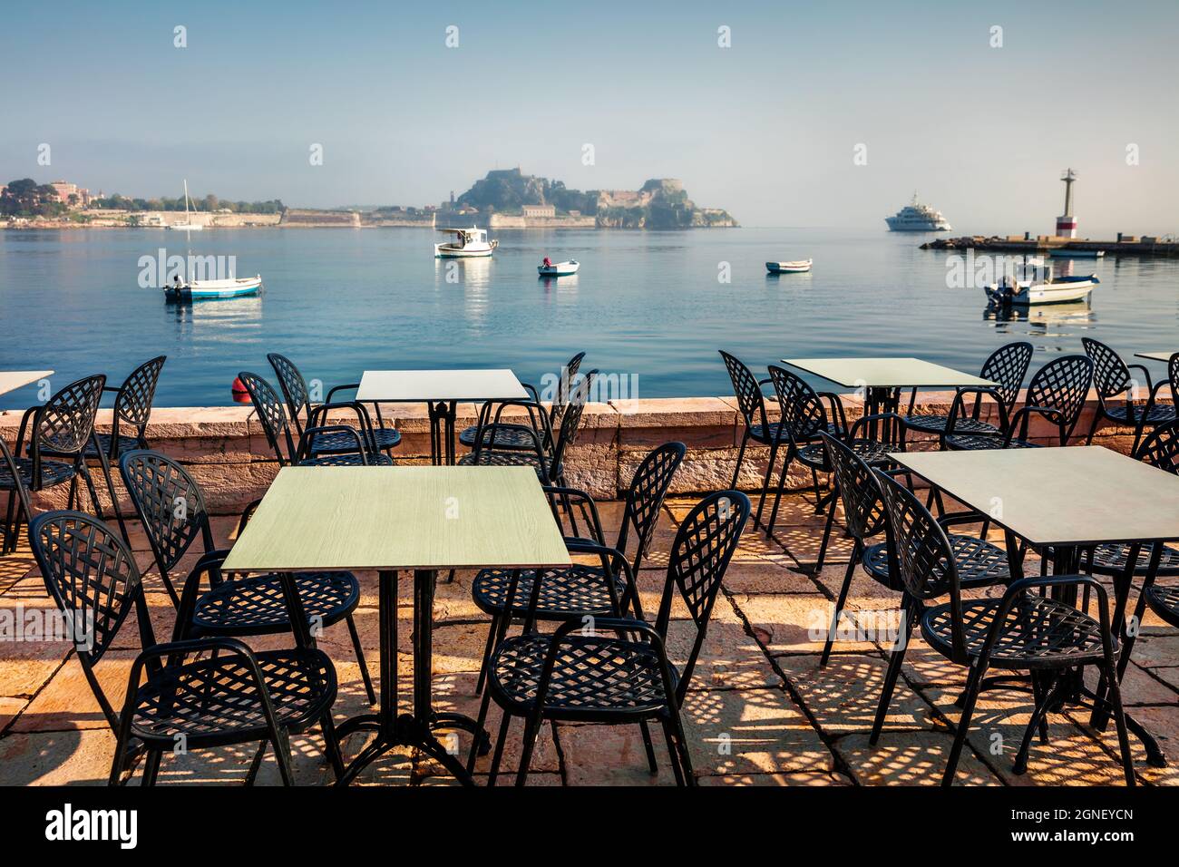 Bella vista mattutina di un accogliente ristorante sul mare con vecchia fortezza veneziana nella città di Kerkira sullo sfondo. Soleggiato mare di primavera del Mar Ionio, Corfù isla Foto Stock