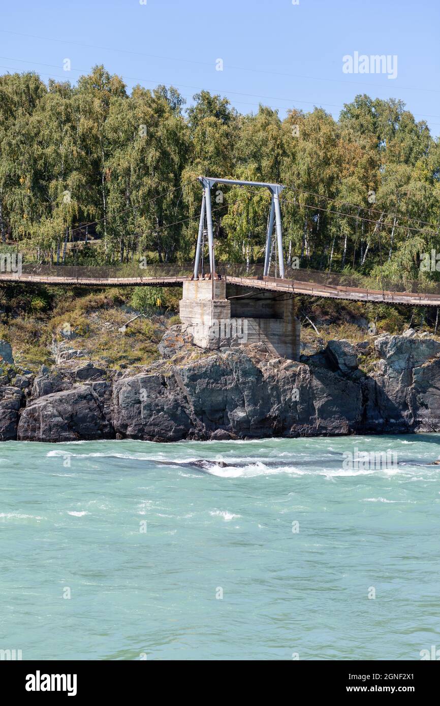 Un ponte sospeso su un ampio fiume in montagna. Foto Stock