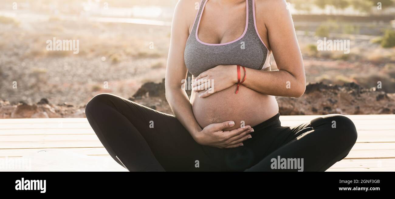Giovane donna che massaggiano il ventre incinta mentre fa la meditazione yoga all'aperto - stile di vita di salute e concetto di maternità Foto Stock
