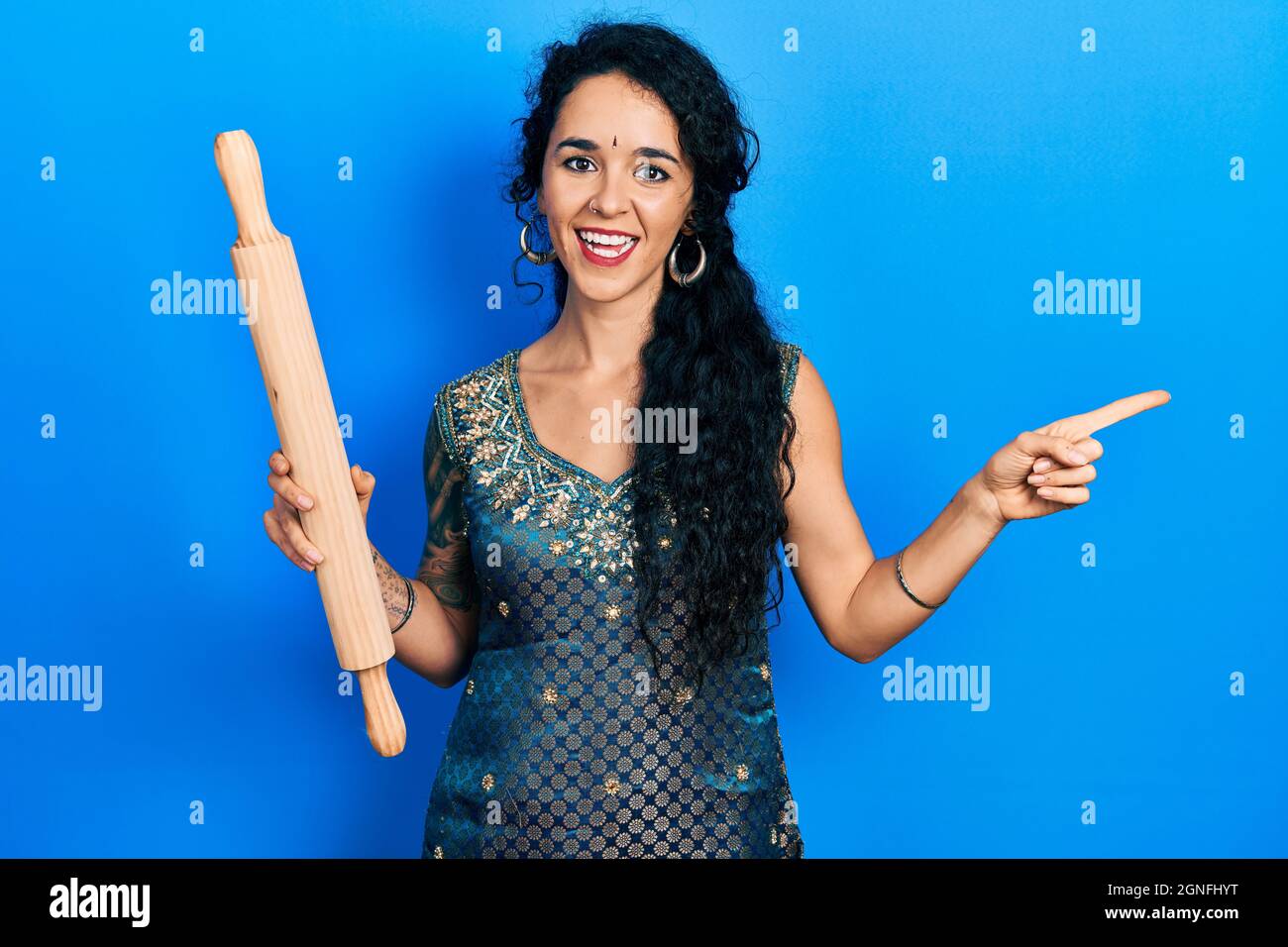 Giovane donna che indossa bindi e tradizionale abito kurta che tiene impastare rotolo sorridente felice indicando con mano e dito a lato Foto Stock