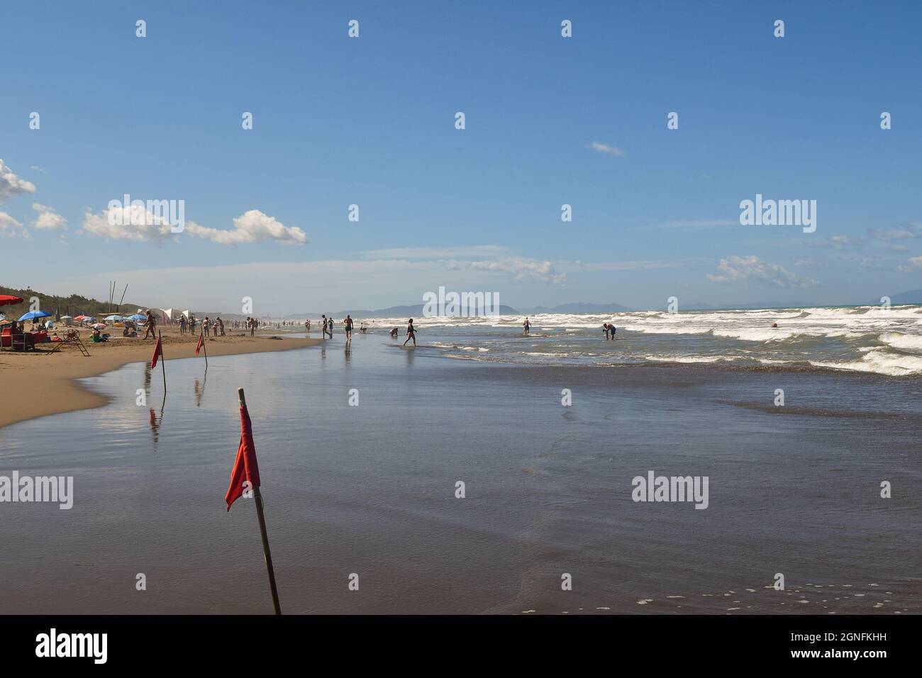 Vista della spiaggia con bandiere rosse in una giornata di mare mosso e grandi onde con gente sulla spiaggia sabbiosa, Marina Castagneto Carducci, Livorno, Toscana Foto Stock