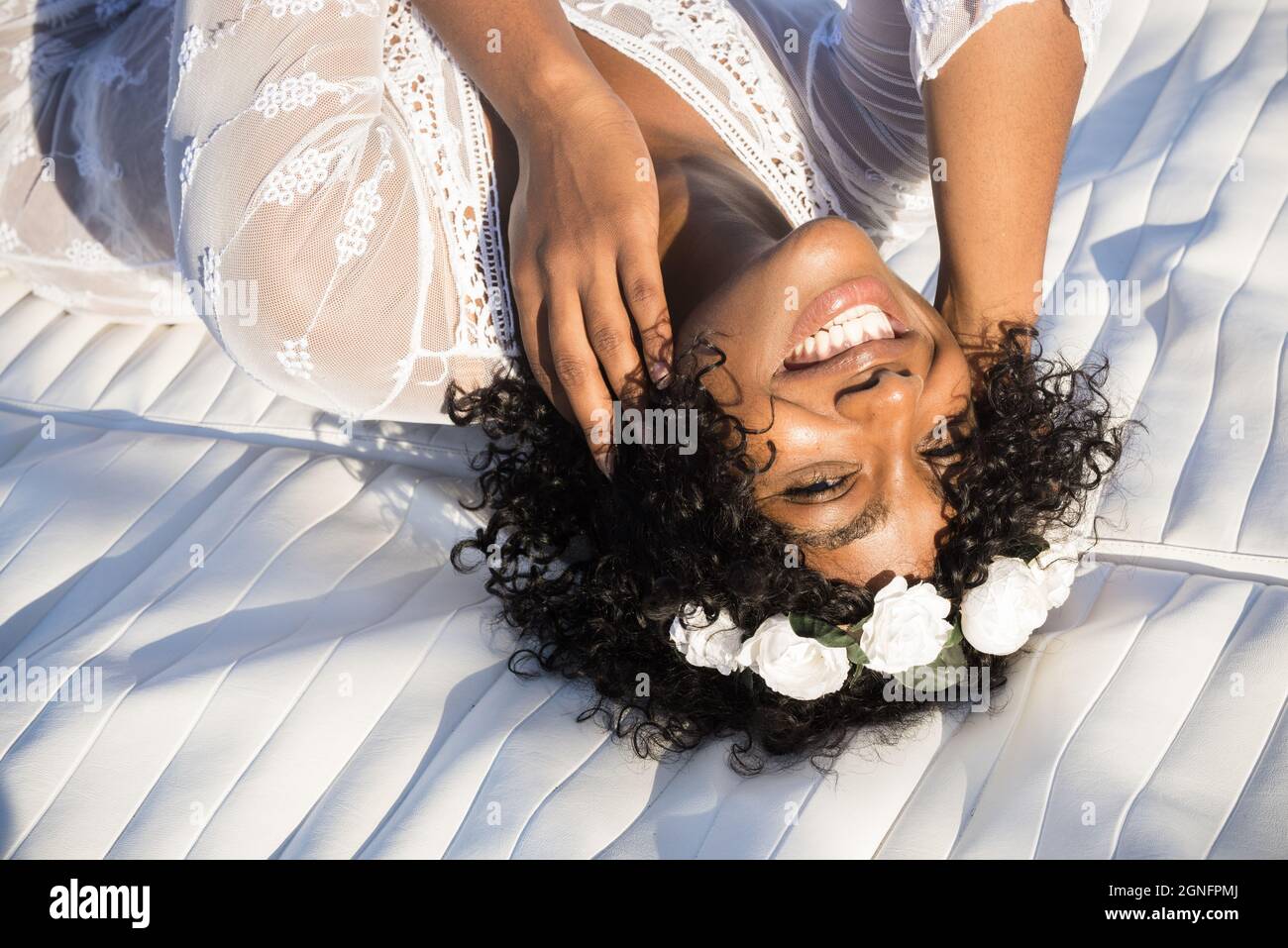 Direttamente sopra lo scatto della donna afro-americana felice con i capelli ricci ed il hairband floreale che guarda in su alla macchina fotografica. Ritratto di gioiosa donna nera in wh Foto Stock