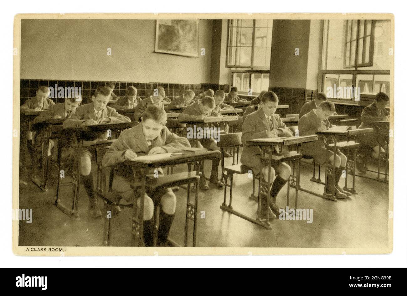Cartolina originale degli anni '30 di ragazzi junior in classe, ragazzi alla scrittura scrivanie, luogo sconosciuto, Regno Unito Foto Stock