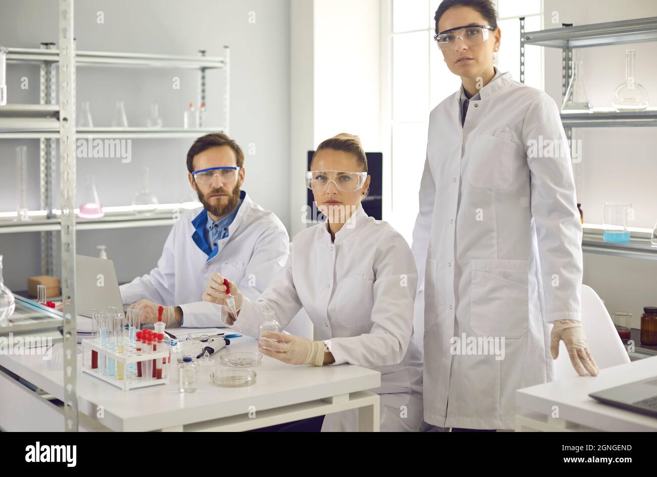 Ritratto di gruppo di giovani scienziati seri in camici da laboratorio e occhiali di protezione nel loro laboratorio Foto Stock