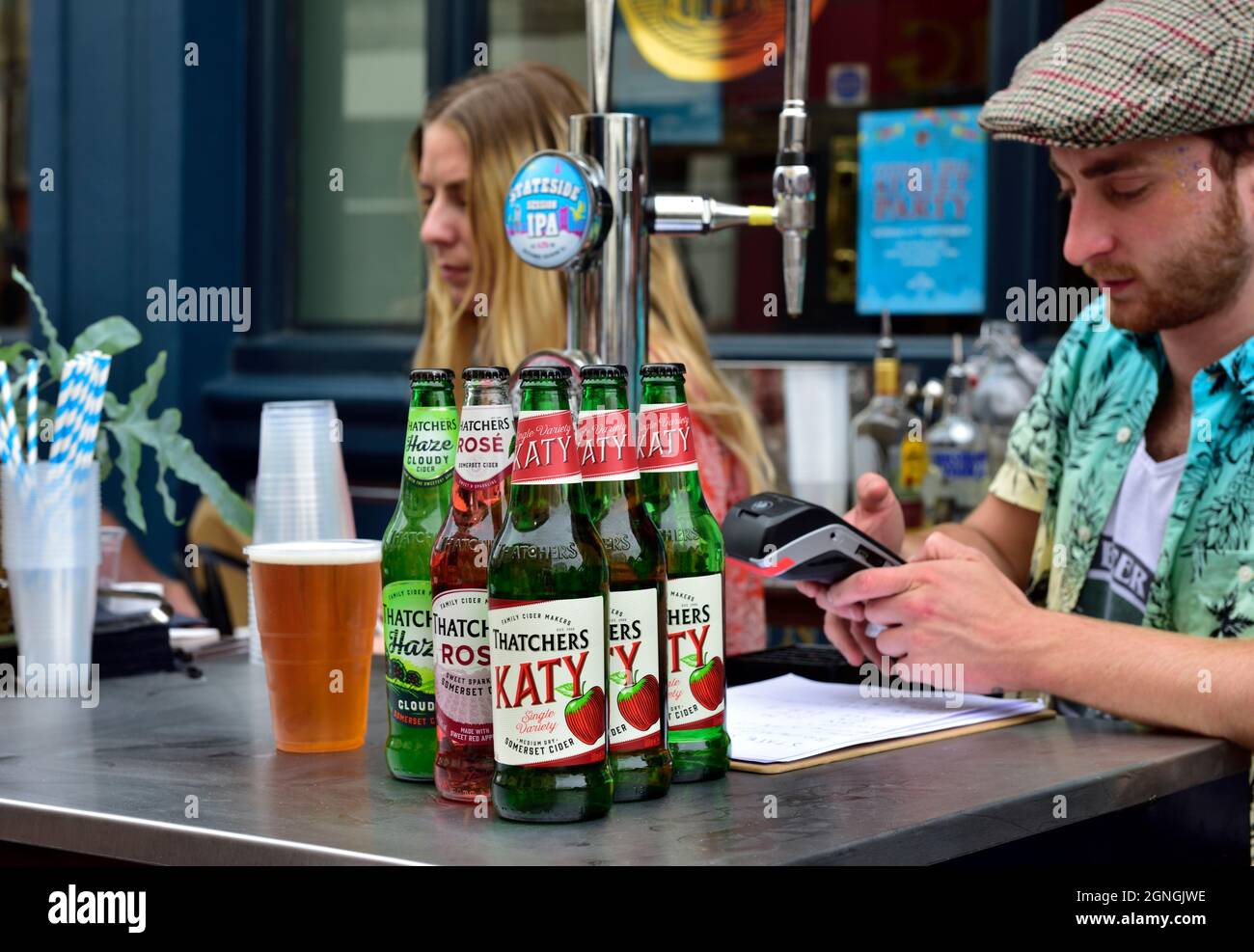 Festa di strada estiva, strada pedonale con caffè, ristoranti e bar fuori sulla strada, uomo con bottiglia di sidro prendendo il pagamento della carta Foto Stock