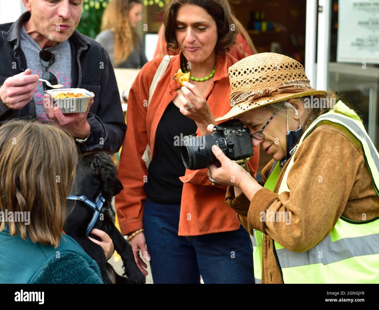 Donna anziana con macchina fotografica che scatta una fotografia di cane tra un gruppo di persone Foto Stock