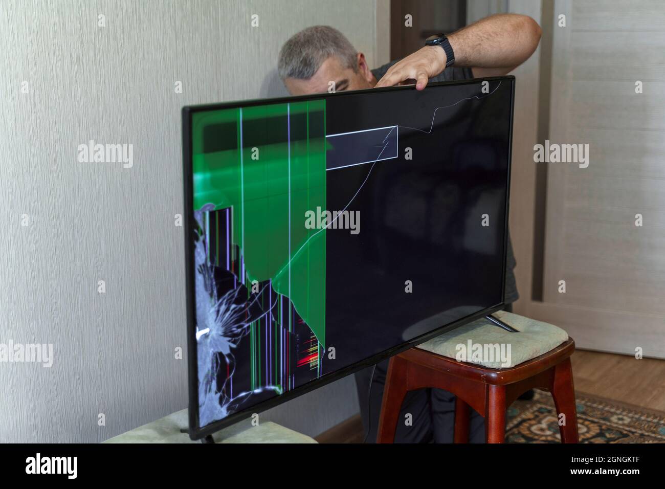 Un uomo che tenta di risolvere un problema di TV. Lo schermo del  dispositivo è rotto Foto stock - Alamy