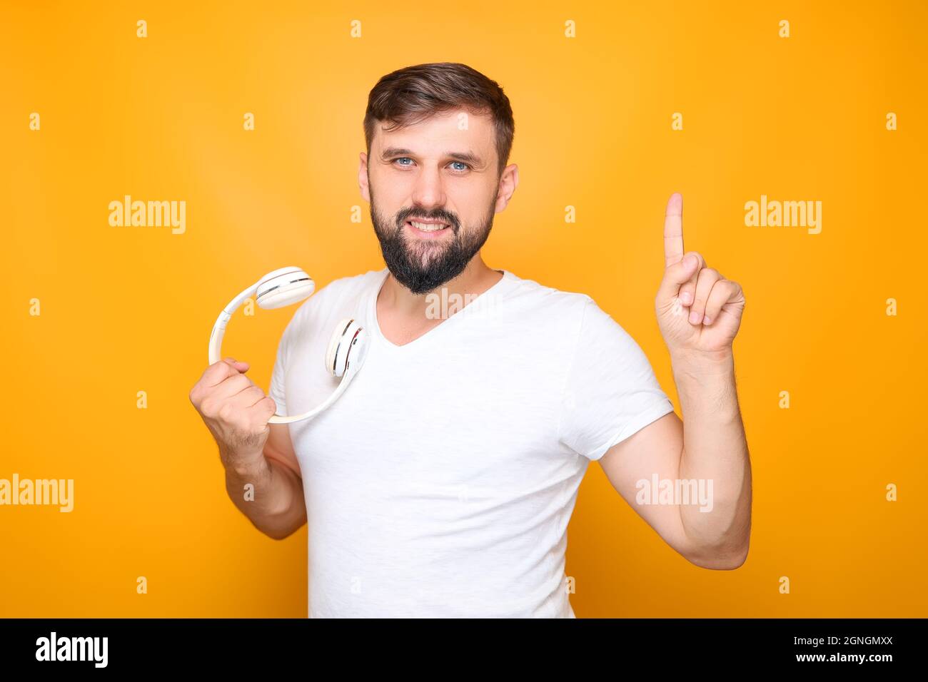 uomo con bearded che tiene in mano cuffie musicali bianche, mostrando i pollici in su. Foto Stock