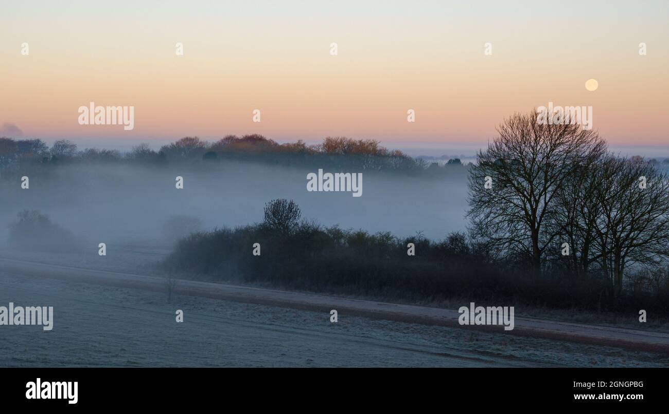 una nebbia mattutina riempì la valle con la luna di neve bassa nel cielo dell'alba Foto Stock